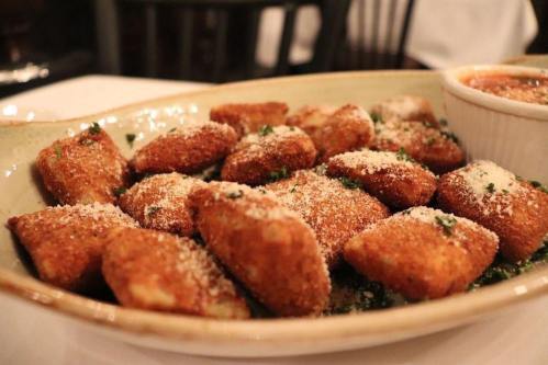 A platter of golden-brown fried bites, sprinkled with cheese and herbs, served with a side of marinara sauce.