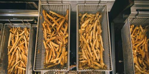 Three baskets of golden, crispy French fries cooling in a commercial kitchen fryer.