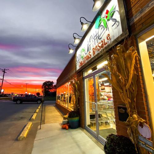 A storefront with a sign reading "Sprout Little" at sunset, featuring decorative corn stalks and pumpkins outside.