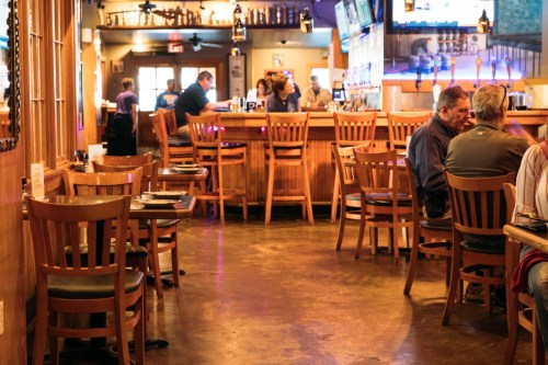 A cozy restaurant interior with wooden chairs, a bar in the background, and patrons enjoying their meals.