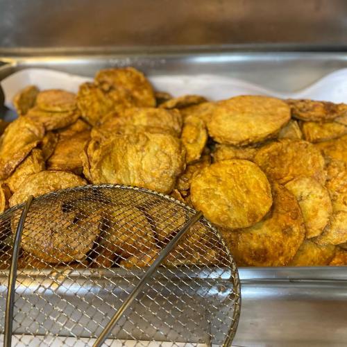 A tray filled with golden-brown, crispy fried potato slices, with a frying basket in the foreground.