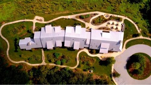 Aerial view of a large building with a metal roof, surrounded by pathways and green landscaping.