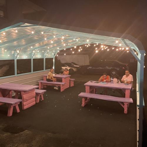 A cozy outdoor seating area with pink tables and string lights, featuring five people enjoying the evening.
