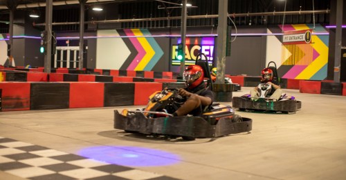 Two go-karts racing on an indoor track with colorful walls and a checkered floor.