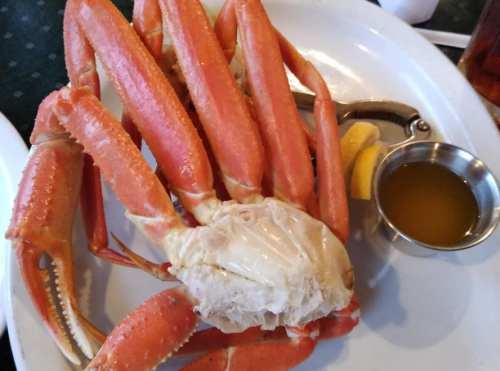 A large crab with orange legs and a piece of crab meat, served with lemon wedges and a small bowl of dipping sauce.