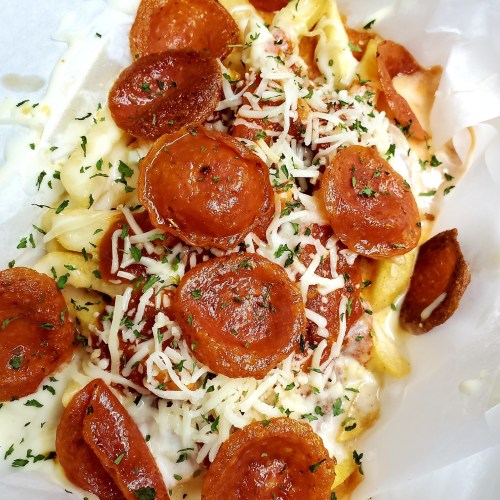 A close-up of loaded fries topped with pepperoni, melted cheese, marinara sauce, and herbs.