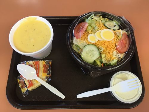 A tray with a bowl of soup, a salad with cheese and vegetables, a small container of dressing, and two crackers.