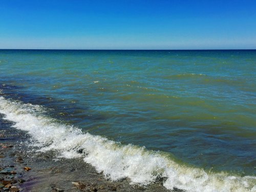A serene shoreline with gentle waves lapping against a rocky beach under a clear blue sky.