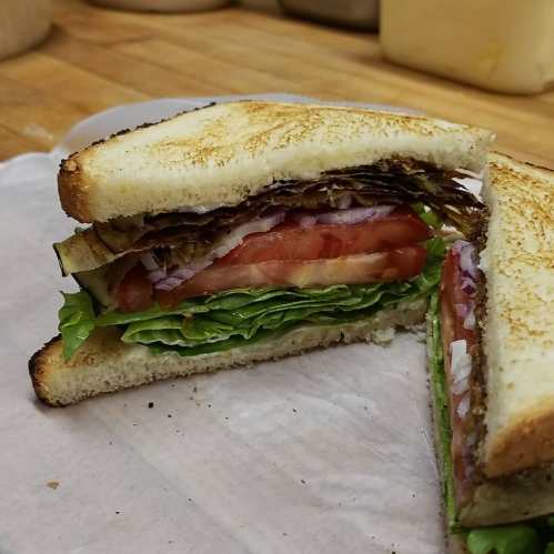 A close-up of a sandwich with layers of lettuce, tomato, and other ingredients, served on toasted bread.