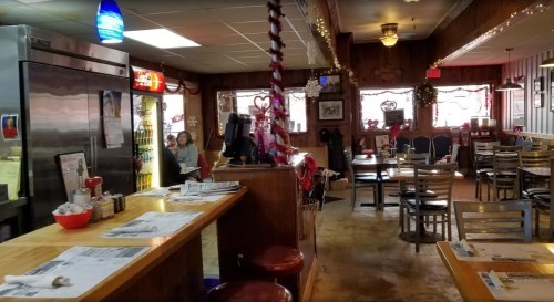 Cozy restaurant interior with wooden decor, tables, and a bar area, decorated for a festive occasion.