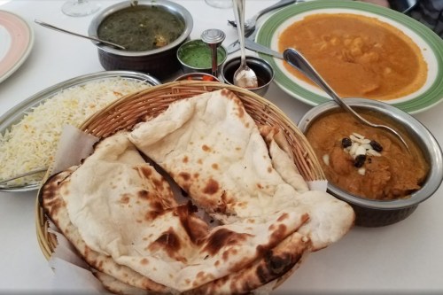 A spread of Indian dishes including naan, rice, and various curries in bowls on a table.