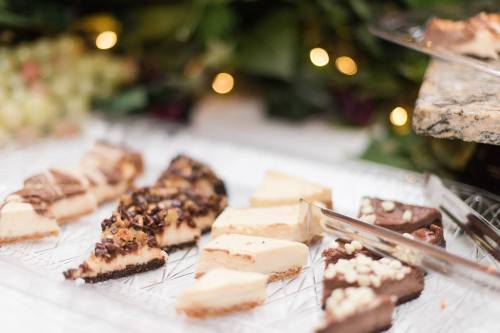 A variety of sliced desserts on a glass platter, featuring different toppings and flavors, with a blurred festive background.