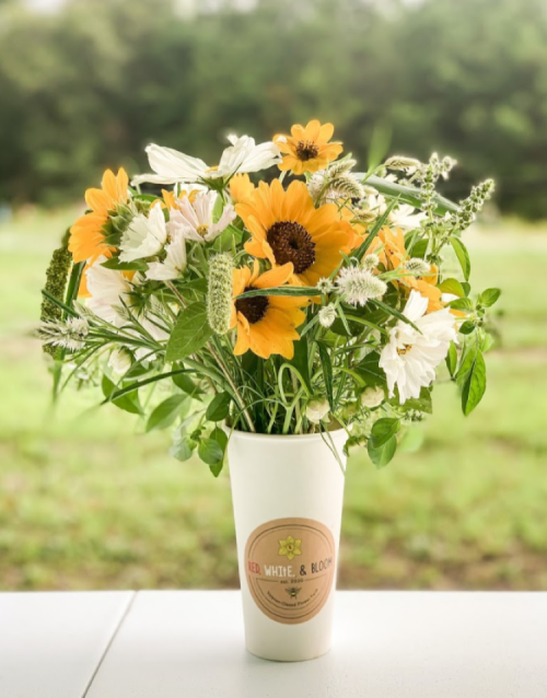 A bouquet of sunflowers and white flowers in a cup, set against a blurred green background.