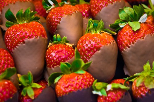 A close-up of fresh strawberries dipped in chocolate, showcasing their vibrant red color and green leaves.