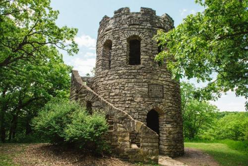 Stone tower with a spiral staircase, surrounded by greenery and trees under a blue sky.
