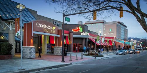 Charleston Town Center entrance with restaurants and shops, illuminated at dusk, alongside a busy street.