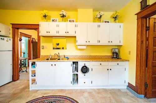 Bright kitchen with yellow walls, white cabinets, granite countertops, and a small laundry area. Flowers decorate the shelves.
