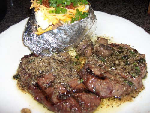 A plate featuring two grilled steak fillets with herbs, accompanied by a baked potato topped with cheese and green onions.