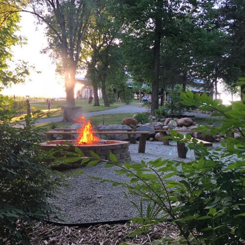 A cozy fire pit surrounded by greenery, with a pathway leading to a gathering area in the background.