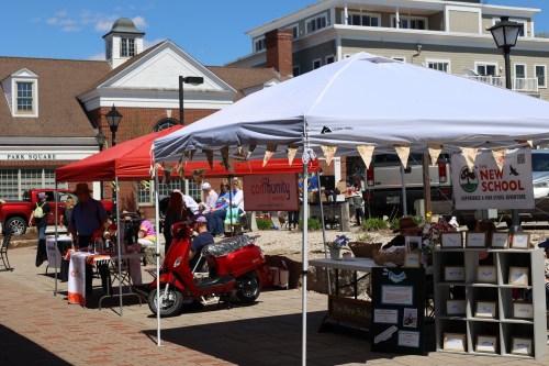 A vibrant outdoor market scene with tents, vendors, and a red scooter, bustling with people enjoying the day.