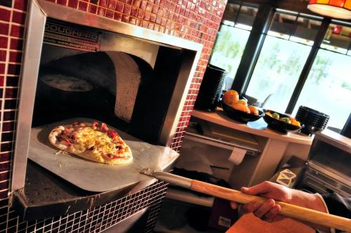 A hand using a paddle to place a pizza into a brick oven in a restaurant kitchen.