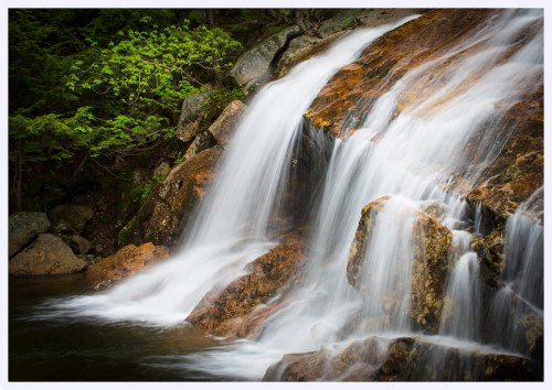 A serene waterfall cascading over rocks, surrounded by lush greenery and a tranquil pool below.
