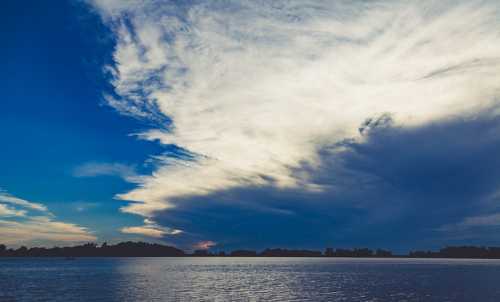 A serene lake scene with a dramatic sky filled with clouds, reflecting soft colors at sunset.