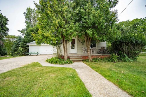 A charming house with a front porch, surrounded by trees and a grassy yard, with a driveway leading to a garage.