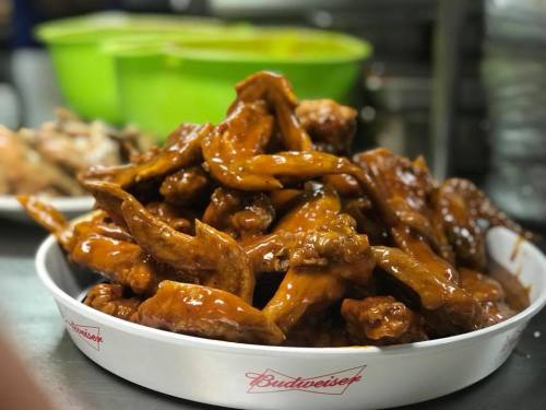 A large plate of glazed chicken wings piled high, with a green bowl in the background.