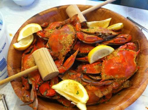 A wooden bowl filled with cooked crabs, garnished with lemon wedges and two wooden mallets for cracking.
