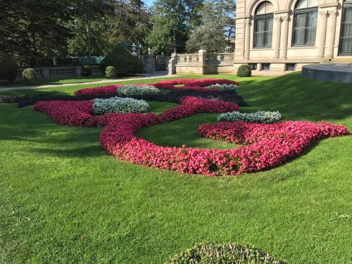 Colorful flower beds arranged in decorative patterns on a lush green lawn near a historic building.