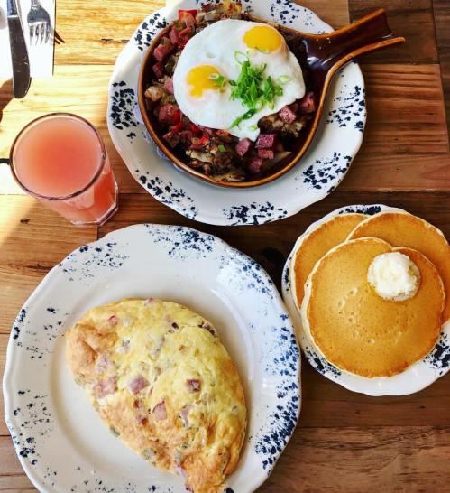 A hearty breakfast spread featuring an omelet, pancakes with butter, and a skillet dish topped with eggs.