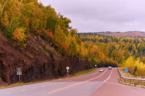 A winding road surrounded by vibrant autumn foliage and rocky cliffs under a cloudy sky.
