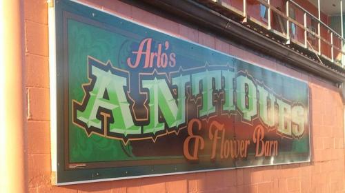 Sign for "Arlo's Antiques & Flower Barn" with colorful lettering on a brick wall.