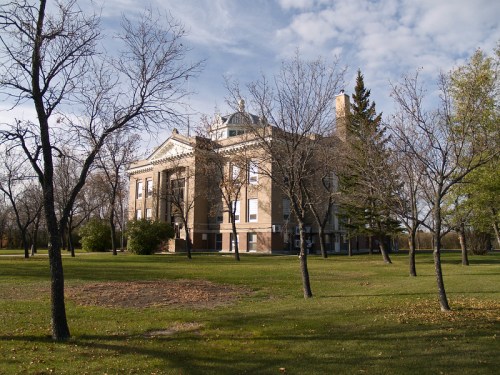Historic building surrounded by bare trees and green grass under a partly cloudy sky.