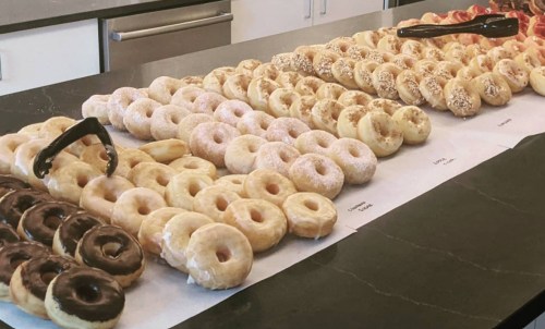 A variety of donuts arranged in rows on a table, including glazed, chocolate, and sprinkled options.