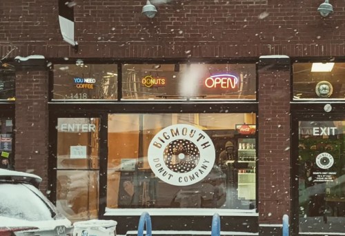 A snowy scene outside Bigmouth Donut Company, featuring a bright "OPEN" sign and a welcoming storefront.