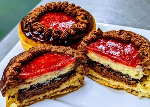Three decadent layered cakes with chocolate frosting, strawberry topping, and creamy filling, displayed on a white plate.