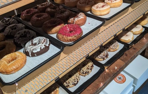 A display of assorted donuts on trays, featuring various toppings and flavors, arranged neatly on shelves.