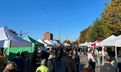 A bustling outdoor market with colorful tents and a crowd of people enjoying the sunny day.