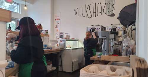 Two employees in a café prepare milkshakes, with a "Thank You" sign on the wall and equipment in the background.