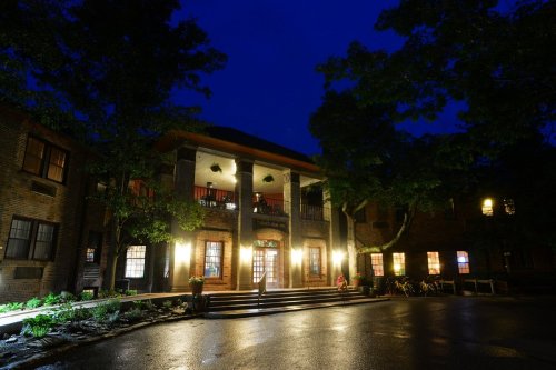 A brick building illuminated at night, featuring a welcoming entrance with steps and surrounding trees.