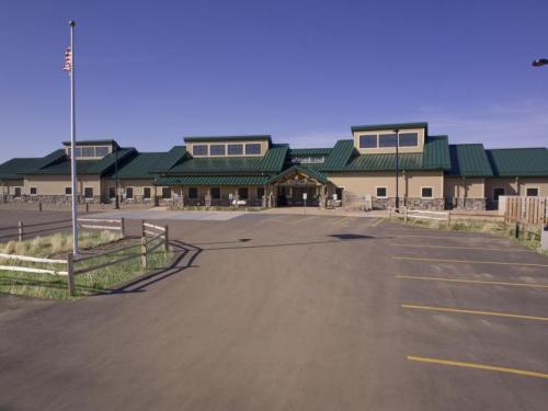 A large building with a green roof, flagpole, and parking lot, set against a clear blue sky.