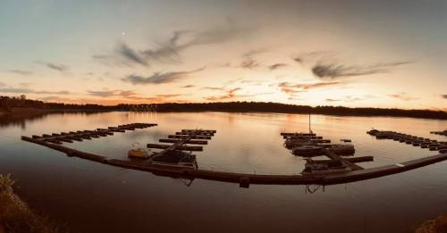 A serene sunset over a calm lake, with boats docked at a marina and colorful clouds reflecting on the water.