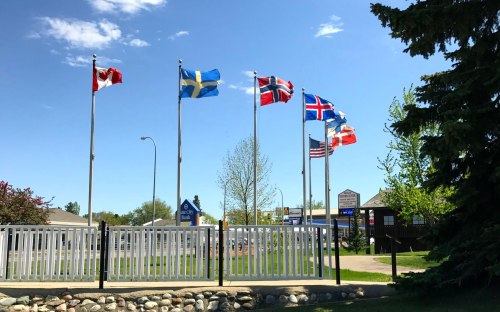 A row of flags from various countries, including Canada, Sweden, Norway, Iceland, and the USA, against a clear blue sky.