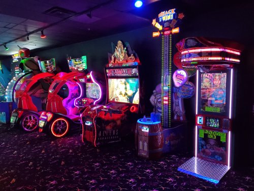 A brightly lit arcade featuring various games, including racing and shooting machines, with colorful neon lights.