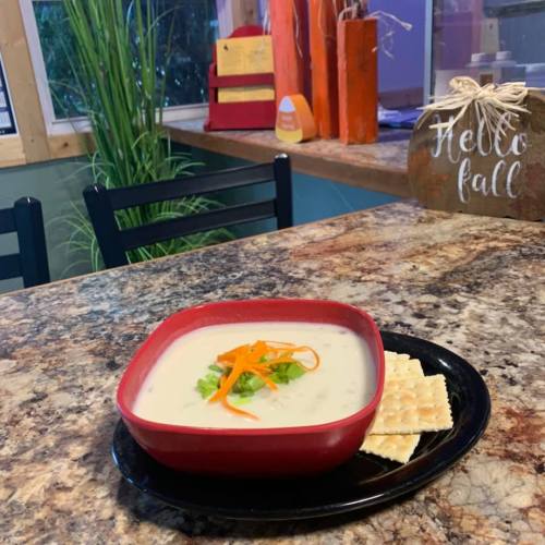 A bowl of creamy soup garnished with green onions and carrots, served with crackers on a black plate.