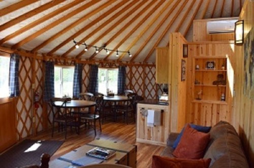 Cozy interior of a yurt featuring wooden beams, tables, and a small kitchenette. Warm and inviting atmosphere.