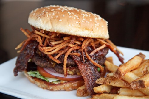 A large burger with crispy fried onions, bacon, lettuce, and tomato, served with a side of golden French fries.