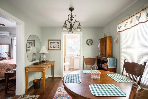 A cozy dining area with a wooden table, checkered placemats, and a view into a bright bathroom.